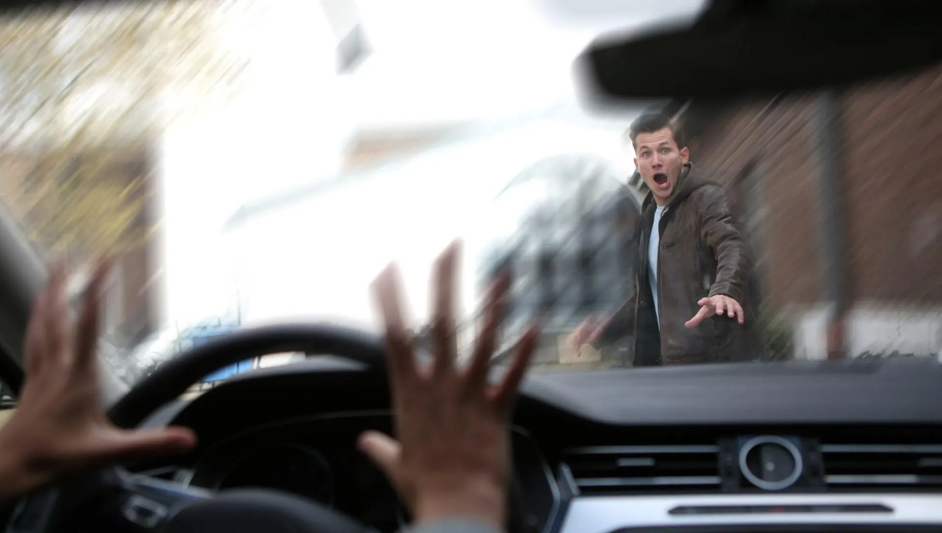 The view through a car windscreen of a pedestrian in the road ahead, with the driver's hands coming off the wheel